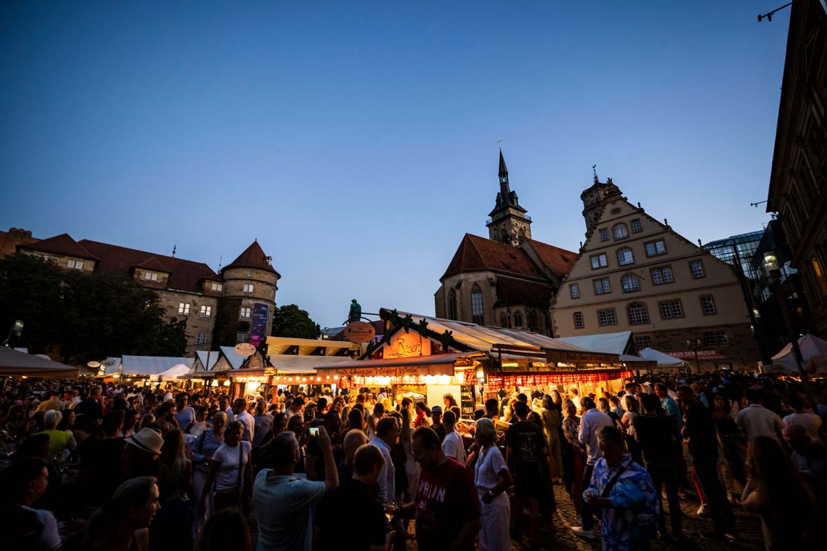 Der Schillerplatz in Stuttgart in der Abenddämmerung, wo die Menschen zwischen den historischen Gebäuden gemeinsam auf dem Stuttgarter Weindorf sind.
